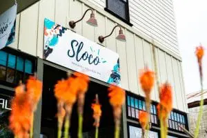 Sloco-Front of Building Flowers and Sign in front of Sloco